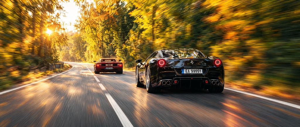 Two classic sports cars driving through a sunlit forest road